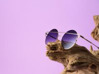 Fashionable sunglasses with purple lenses placed on timber. in purple background